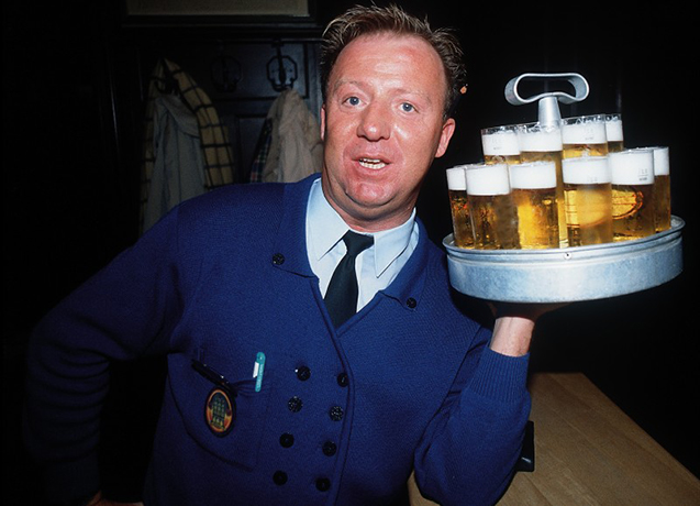 De obers in Keulen dragen een wit hemd, zwarte broek, blauw schort en blauwe das, de laatste weggestopt van de schuimende glazen K&ouml;lsch.